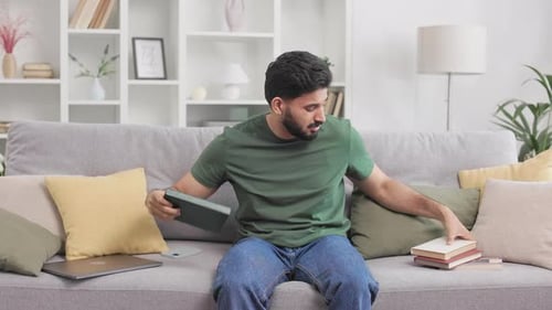 Frustrated Young Man With Books Sits On Sofa
