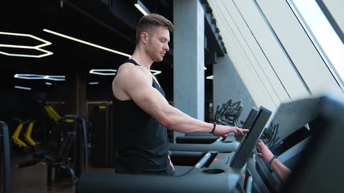 Sportsman on a treadmill. Handsome guy starts training on a simulator in modern fitness club.