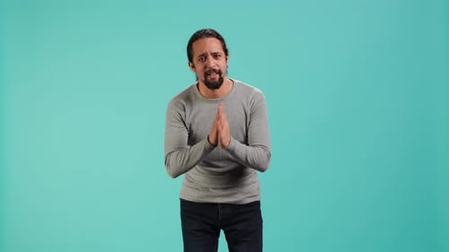 Man Pleading with Hands Clasped on Blue Backdrop
