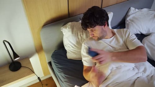 Vista superior de un hombre de pelo negro que usa un teléfono inteligente a altas horas de la noche apaga la luz y va a