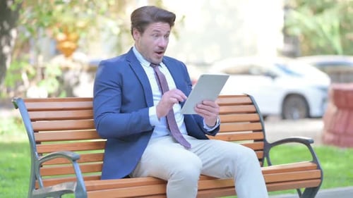 Excited Man Using Tablet Sitting on Bench