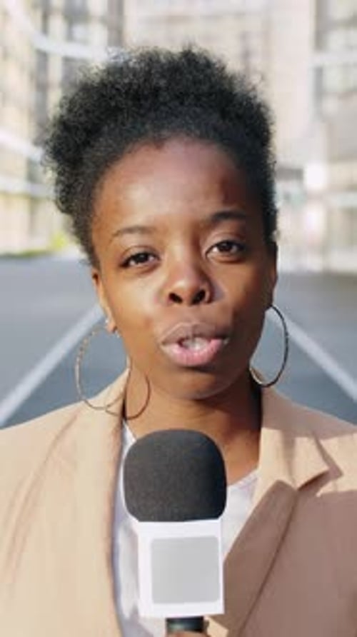 Woman Reporter Speaking into Microphone in City Environment
