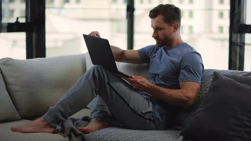 Man Relaxing on Sofa Using Laptop Computer Indoors
