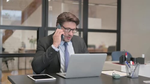 Businessman Talking on Phone While Using Laptop