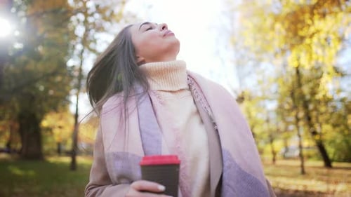 Portrait of Caucasian Beautiful Young Woman Going Forward in Park with Glass of Coffee and Drinking
