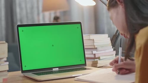 Close Up Of A Mock Up Green Screen Laptop Being On A Table While A Female Writing On The Book