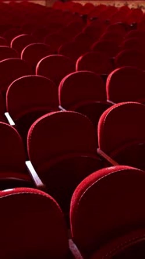 Rows of empty red velvet seats inside a theater or opera. No people in hall because of pandemic.