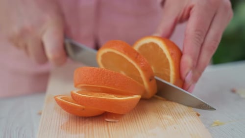 Nahaufnahme kaukasischer Hände, die Orange auf einem Holzbrett in Scheiben schneiden, helle Zitrussegmente, die morgens aufgefächert sind