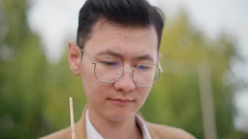 Young Asian Man Sketches Outdoors Street Artist in Peaceful Park Setting Focused Young Asian Male