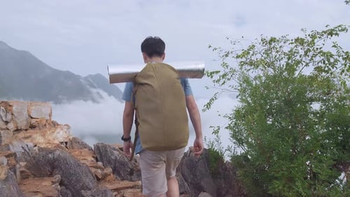 Caminhante asiático masculino com uma mochila caminhando em uma montanha nebulosa