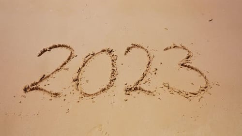 Meereswellen spülen die Inschrift von 2023 auf Sand weg