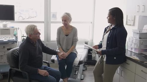 Doctor Talking to Senior Couple Holding Hands in Clinic Exam Room 10 Seconds or Greater