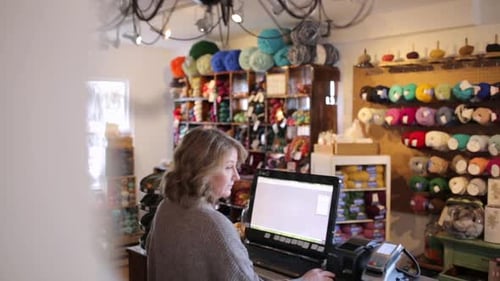 Mature woman purchases wool at yarn store counter transaction in retail shop