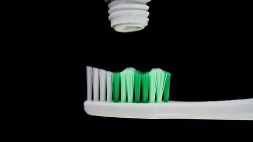 A toothbrush being loaded with some toothpaste, dark background.