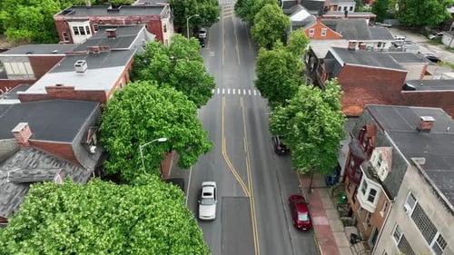 Aerial Birds Eye shot in America neighborhood with green trees. Driving cars on quiet road in small