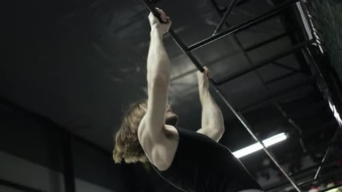 Langhaarige in Sportkleidung beim Aufführen von Klimmzügen an einer Metallstange im Fitnessstudio