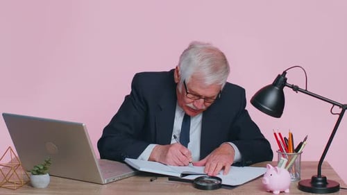 Senior Man Writing Notes at Desk in Office