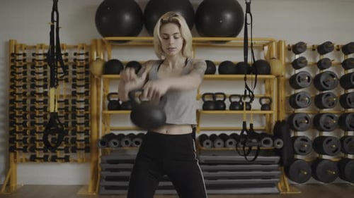 Young woman lifting kettle bell in gym