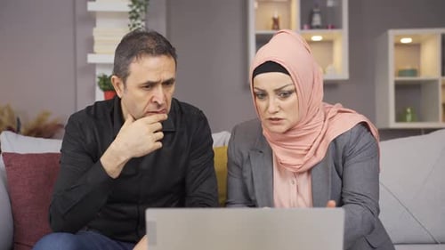 Concerned Couple Works on Laptop Together on Sofa