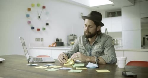 Man writing on adhesive note besides laptop in kitchen