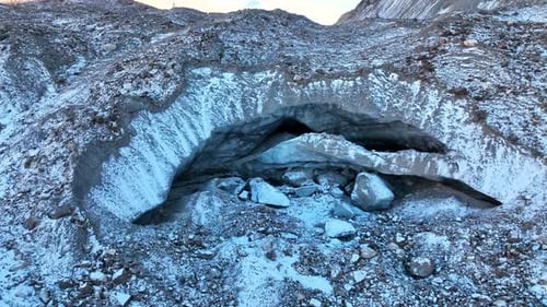Entrance to a small ice cave or meltwater tunnel on a rocky slope