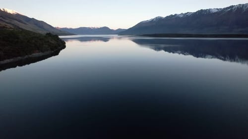 Aerial flying over Lake Wakatipu with the lake surrounded by snow capped mountains reflecting in the