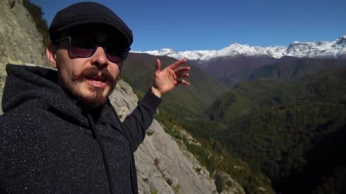Mann mit Sonnenbrille und Mütze steht auf einem hohen Berg und spricht über Landschaften und verschneite Gipfel