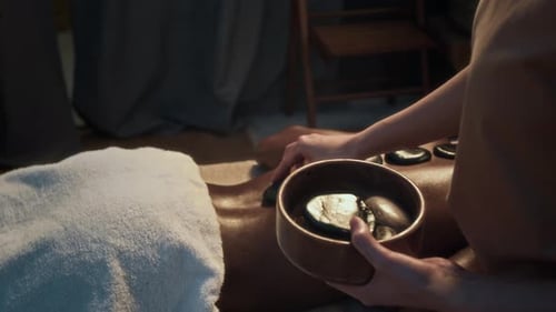 Unrecognizable Masseuses Hands Placing Hot Stones Onto Back of Black woman