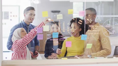 Group of diverse business people taking notes on glass wall and talking in office, slow motion