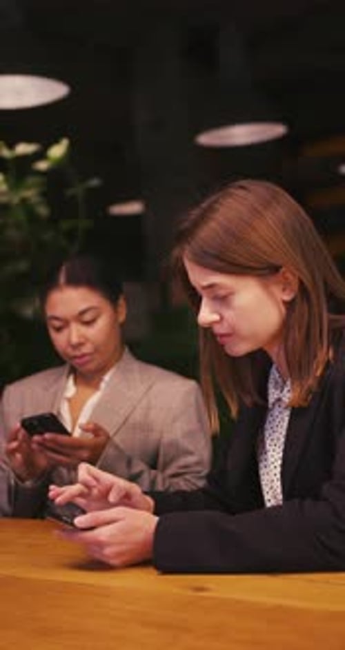 Two Young Women Using Phones at a Table