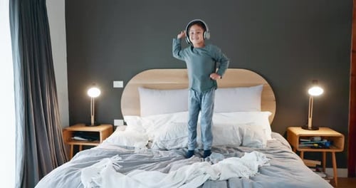 Child Happily Jumps on Bed With Headphones On