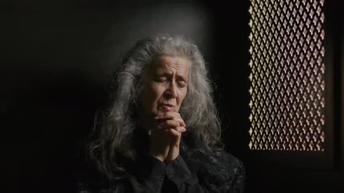 Elderly Woman Praying Alone in Confessional Booth