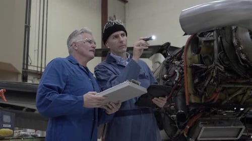Male Airplane Mechanics Inspecting Engine In Hangar