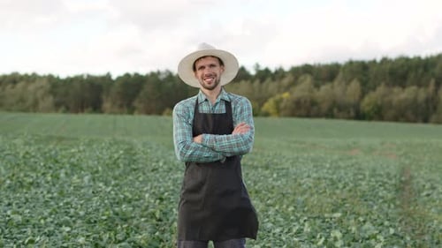 Male Farmer Stands in Field with Plants and Smiles Pleased with Work Done