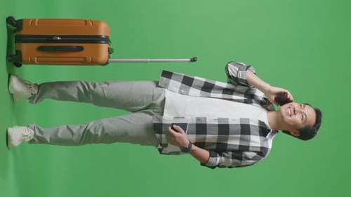 Full Body Of Asian Male Traveler With Luggage And Passport Talking On Smartphone In The Green Screen