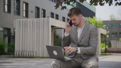 Young Man Working Outdoors on Laptop Talking on Phone