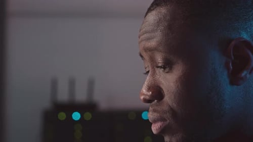 Focused Man in Dark Server Room Looking Thoughtful