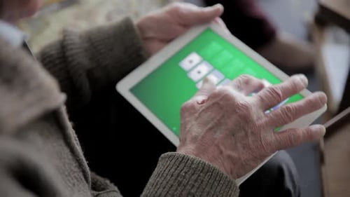 Homme âgé appréciant un jeu de solitaire sur tablette numérique à l'intérieur pendant sa retraite