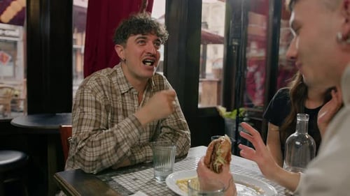 Wide shot - a group of friends chatting at a table in a restaurant, eating a burger and french fries