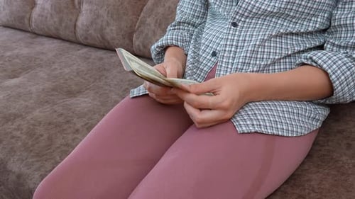 Woman Counts Stack of US Currency on Couch