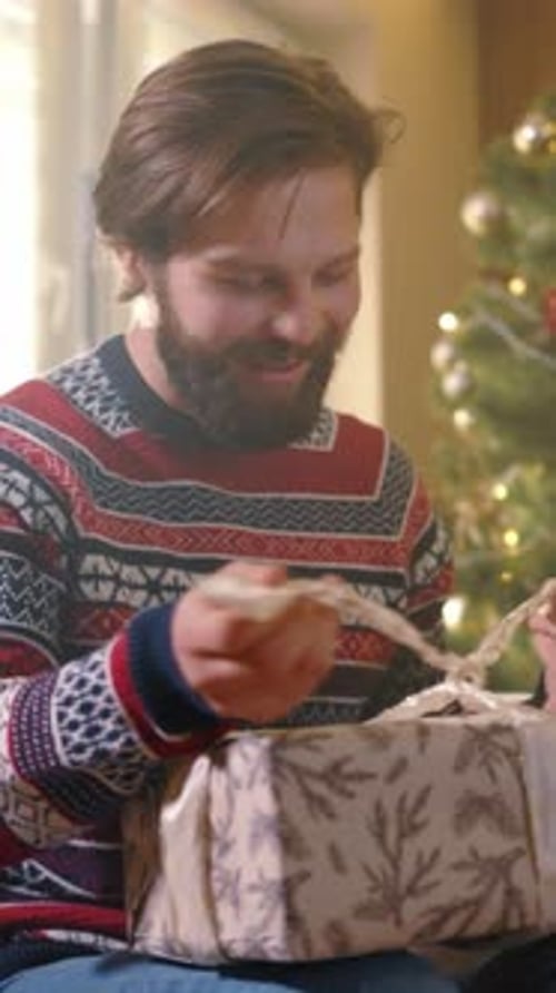 Man Unwrapping Christmas Present in Living Room