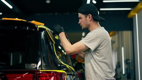 Autodetails an einer Tankstelle Das schwarze Auto ist mit gelbem Klebeband bedeckt, der Prozess des Polierens