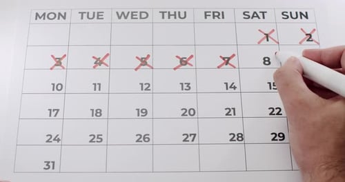 Hand Marking off Dates on Calendar with Red Marker