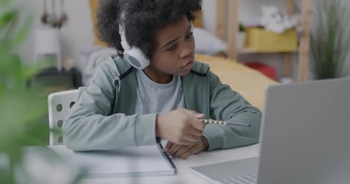 African American Boy Studying in Online School Having Virtual Meeting with Teacher Writing in