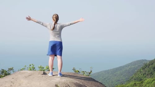 Young woman raising hands on top of mountain