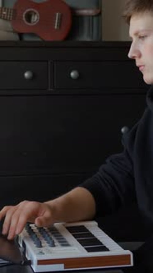 Young Man Creates Music with Laptop and Keyboard
