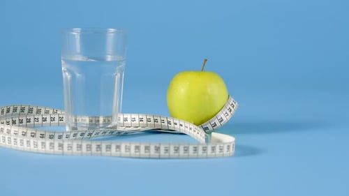 Transparent Glass and Green Apple with Measurement Tape at Blue Background
