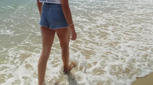 Young Woman Walking Along Beach with Hair Blowing in the Wind In