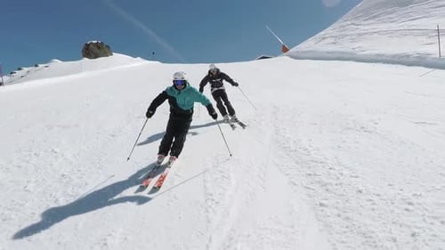People Skiing Down a Snowy Mountain Slope on Sunny Day