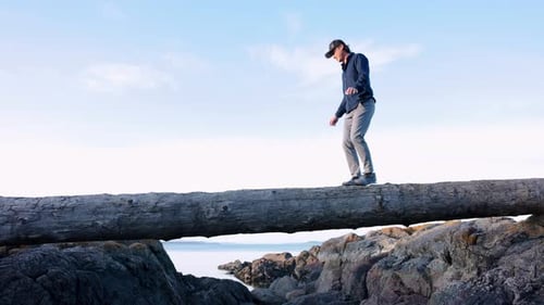 Man Balancing on Log Over Rocky Beach Coast